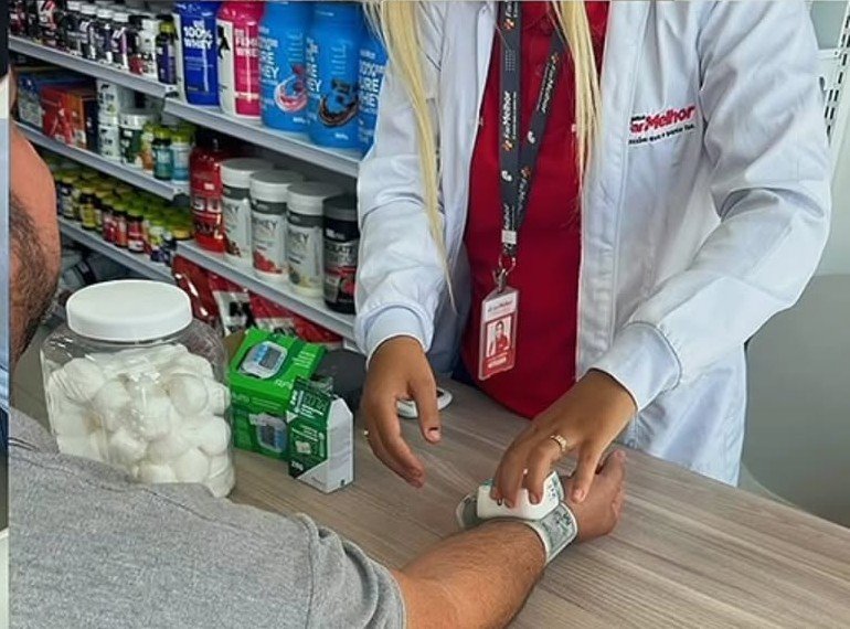 Farmacêutica de jaleco branco aferindo a pressão de um cliente no balcão da loja